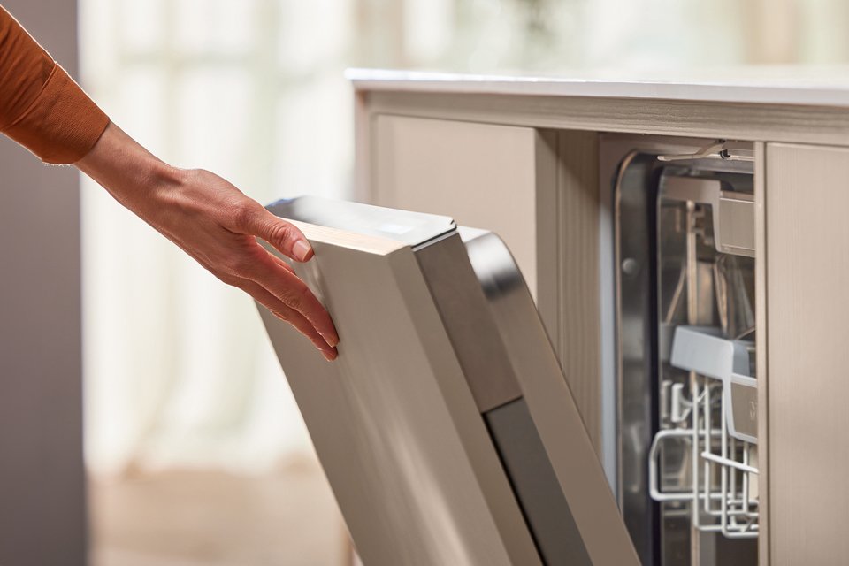 Built-in Miele Dishwasher door being opened by a hand.